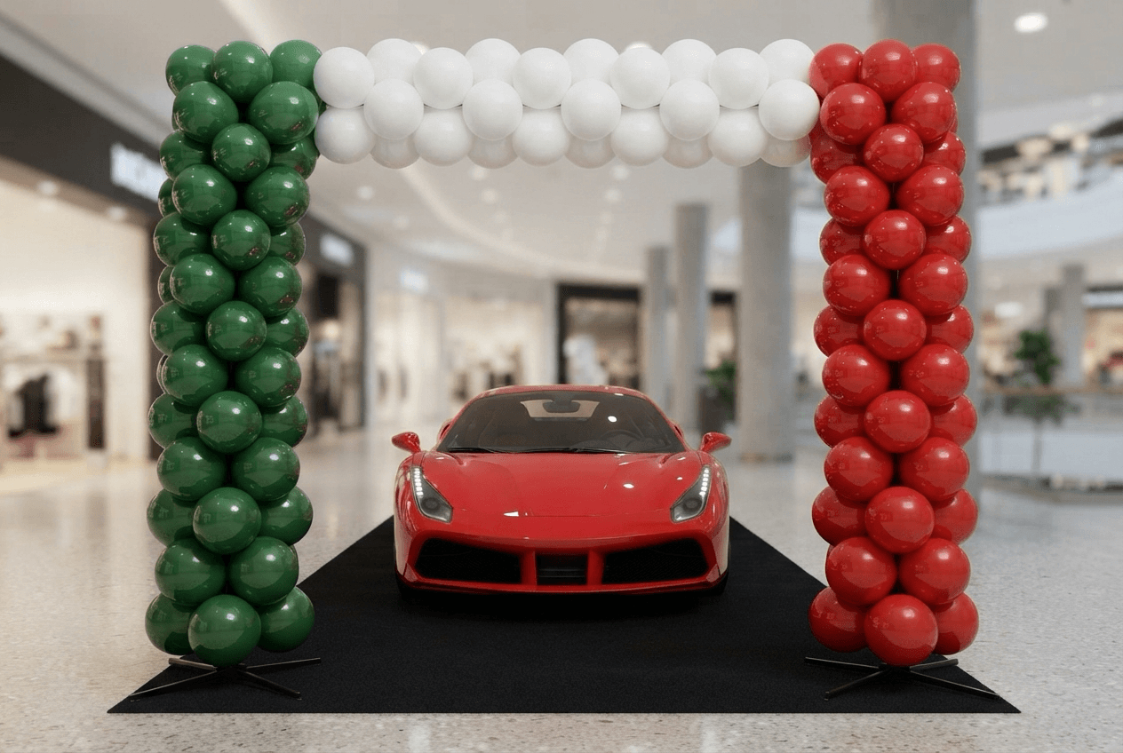 Ballonnenpilaren in groen, wit en rood met een boog erboven rond een rode sportwagen in de showroom