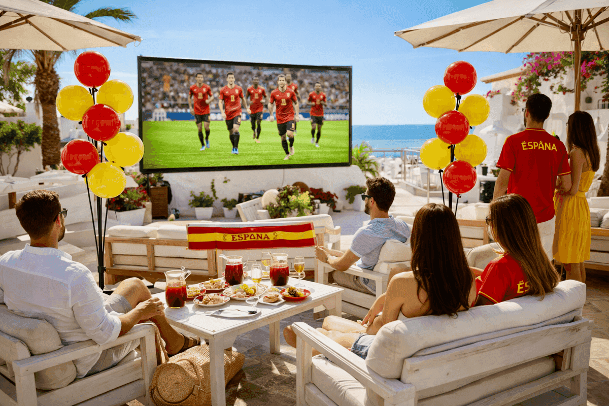 Rode en gele ballonpilaren op een zonnig terras bij een groot scherm tijdens een voetbalwedstrijd