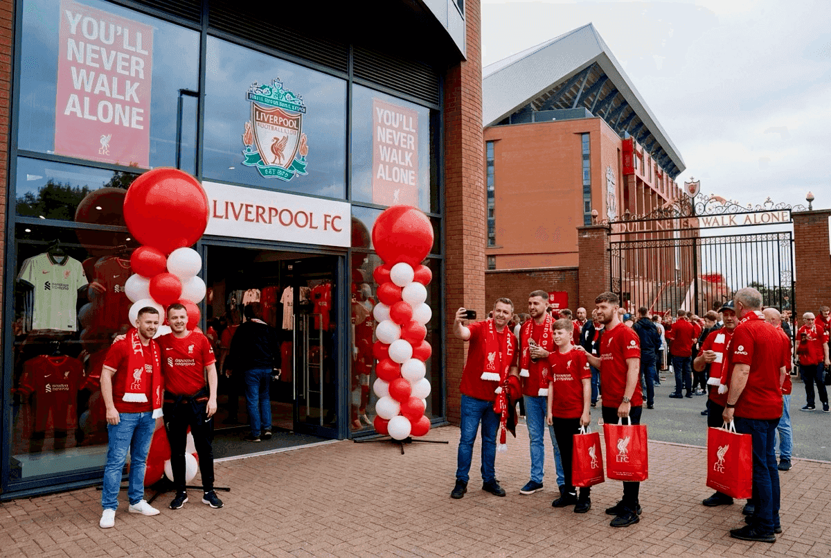 Rood-witte ballonpilaren bij de ingang van een clubfanshop met supporters die foto’s maken