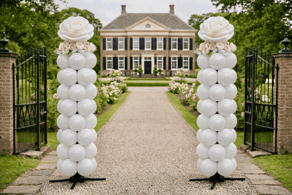 Twee witte ballonpilaren met roze bloemen bij landhuis entree